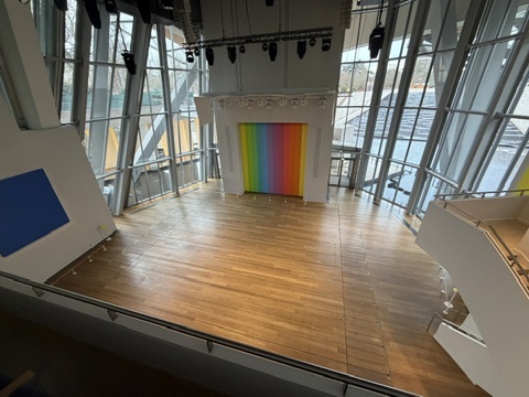 Vue en hauteur de l’auditorium de la Fondation Louis Vuitton, avec parquet, baies vitrées et œuvre multicolore.